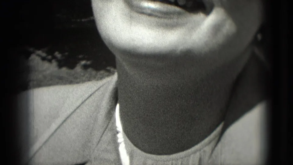 Close-up 1975 home-movie frame of a smiling woman near the camera, cropped tightly at the face and shoulder.