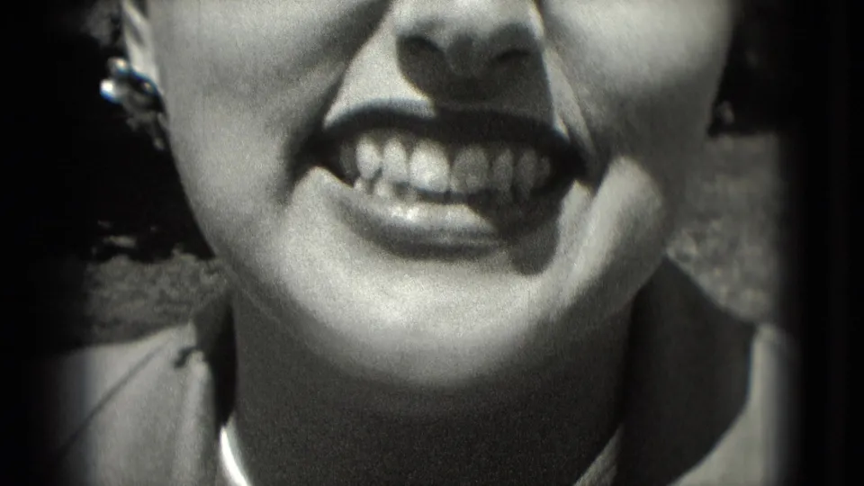 1975 Washington, DC home-movie close-up of an adult woman grinning broadly, with styled hair, earrings, and strong sunlight on her face.
