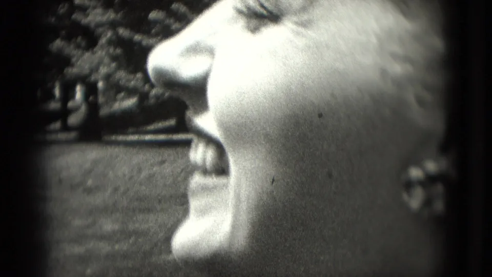 Close-up of a smiling woman in profile, likely from a 1975 Washington DC 8mm home movie, with trees in the background.
