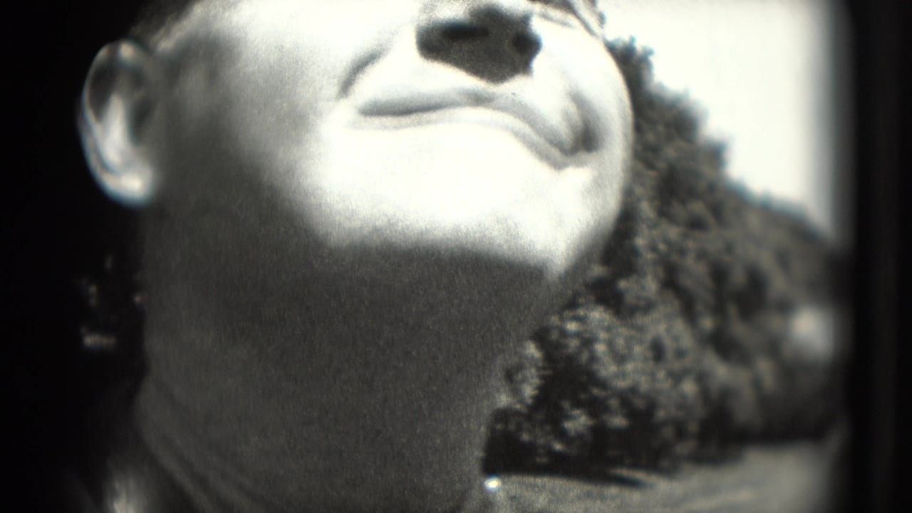 Tight close-up of a smiling man's face in a 1975 Washington DC home-movie frame, with outdoor foliage behind him.