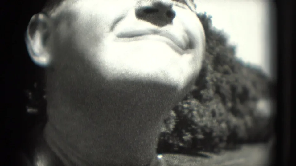 Tight close-up of a smiling man's face in a 1975 Washington DC home-movie frame, with outdoor foliage behind him.