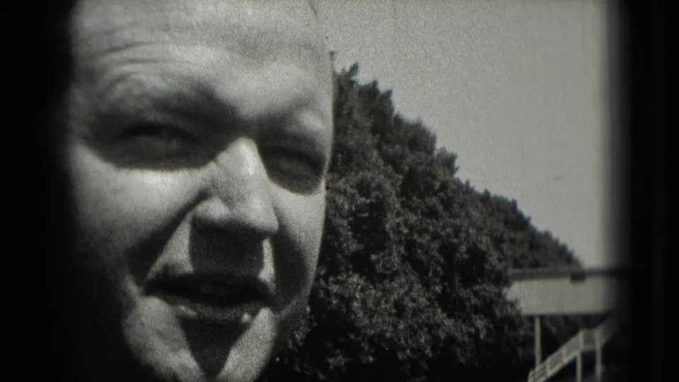 1975 Washington, DC home-movie close-up of a man in a cap smiling in bright outdoor light, with trees behind him.