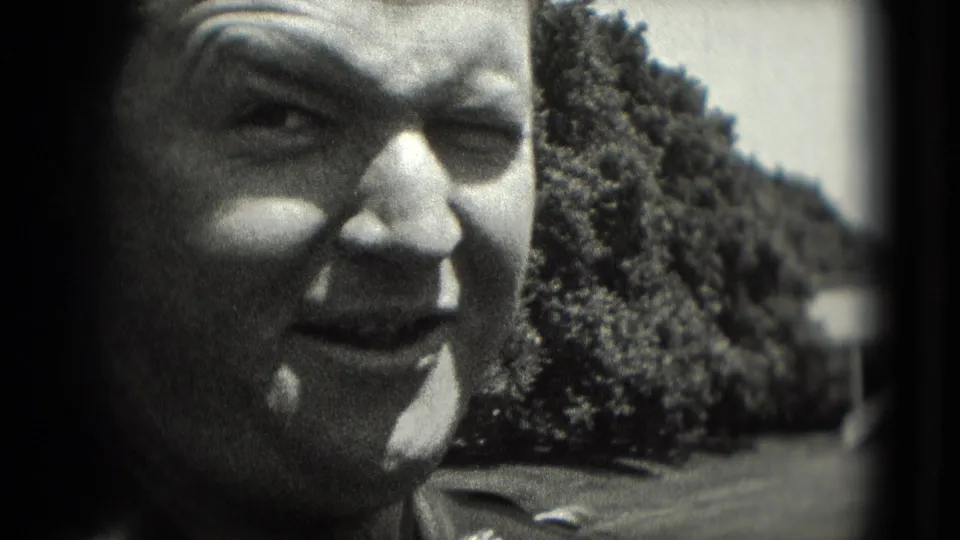 Black-and-white 8mm close-up of a man in uniform-style clothing squinting outdoors in Washington, DC in 1975.