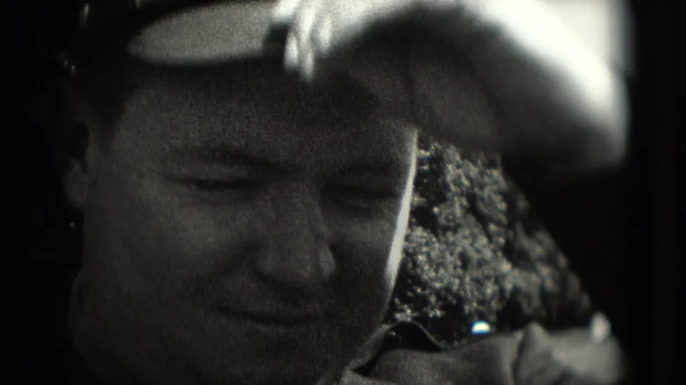 A uniformed man appears to adjust his cap in a soft, grainy 1975 Washington, DC home-movie close-up.