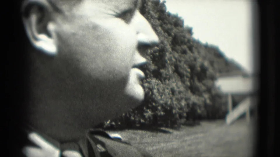 Close 8mm frame of an adult man in profile at a Washington, DC outdoor amusement setting, with trees and ride structures behind him.