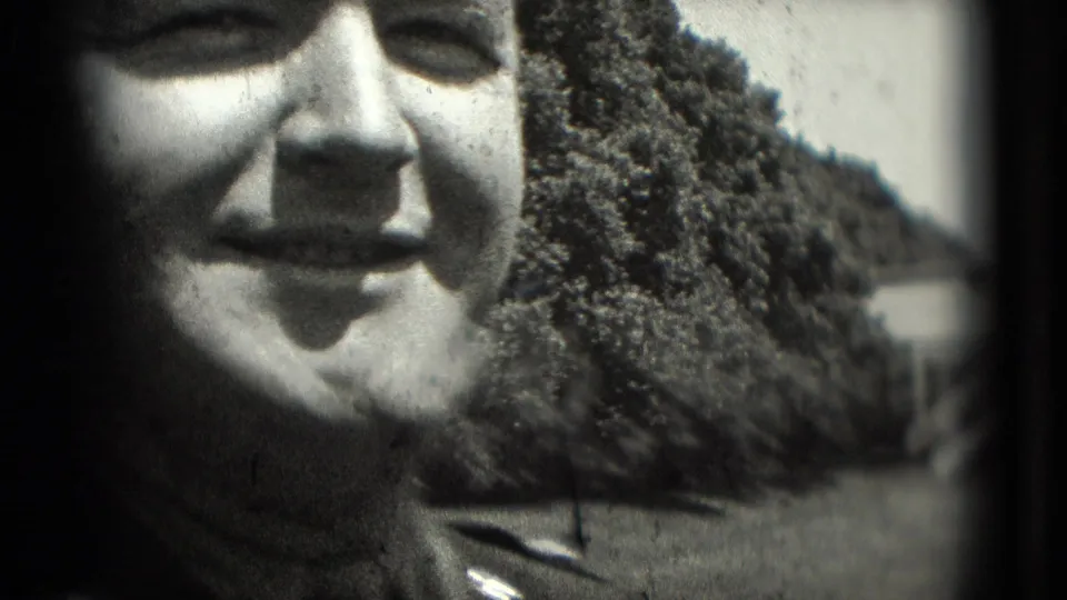 Close home-movie frame of an adult face in a bright outdoor amusement setting in Washington, DC, with trees and structures behind.
