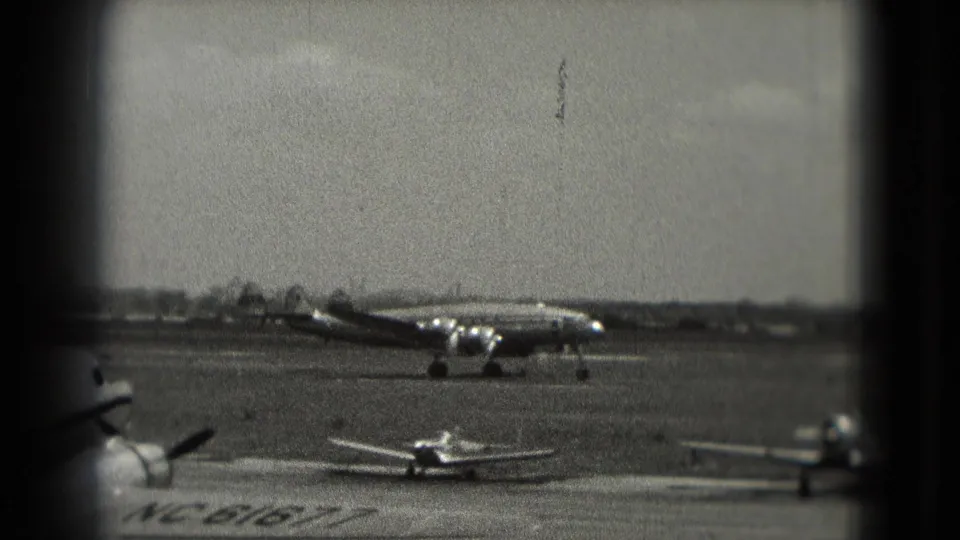 1975 Washington DC airport view with a propeller airliner taxiing past smaller planes on an open tarmac.