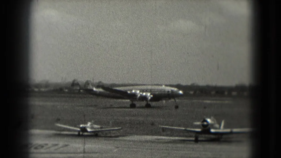 1975 Washington DC home-movie frame showing a taxiing propeller airliner behind smaller aircraft on the tarmac.