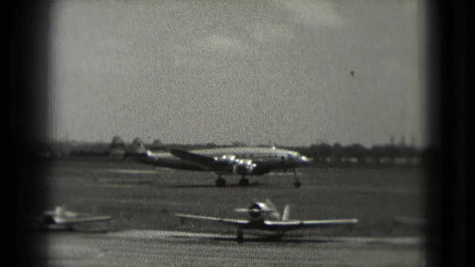 1975 Washington DC 8mm view of a propeller airliner on the tarmac with small aircraft in the foreground.