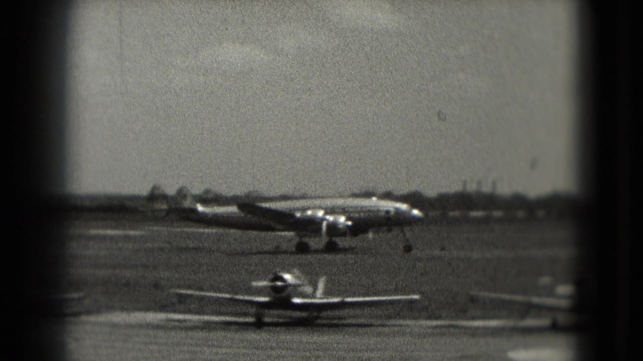 Large propeller aircraft taxiing behind small parked planes on an airfield runway.