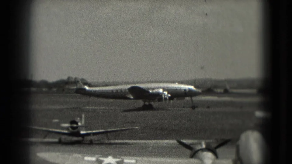 Grainy 1975 Washington, DC 8mm frame showing the propeller aircraft farther along the runway with a small plane below it.
