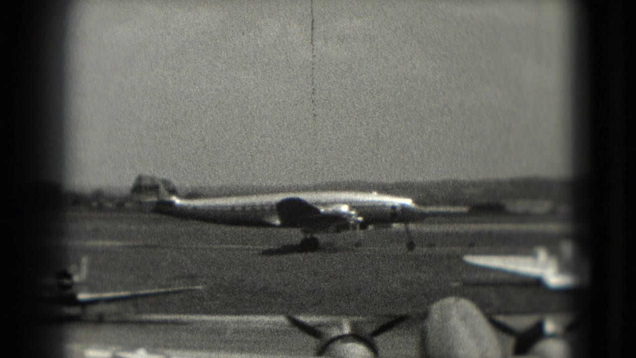 1975 Washington, DC airport footage showing a large propeller aircraft across the runway, framed by dark 8mm gate edges.