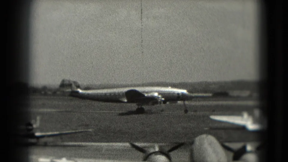 1975 Washington, DC airport footage showing a large propeller aircraft across the runway, framed by dark 8mm gate edges.