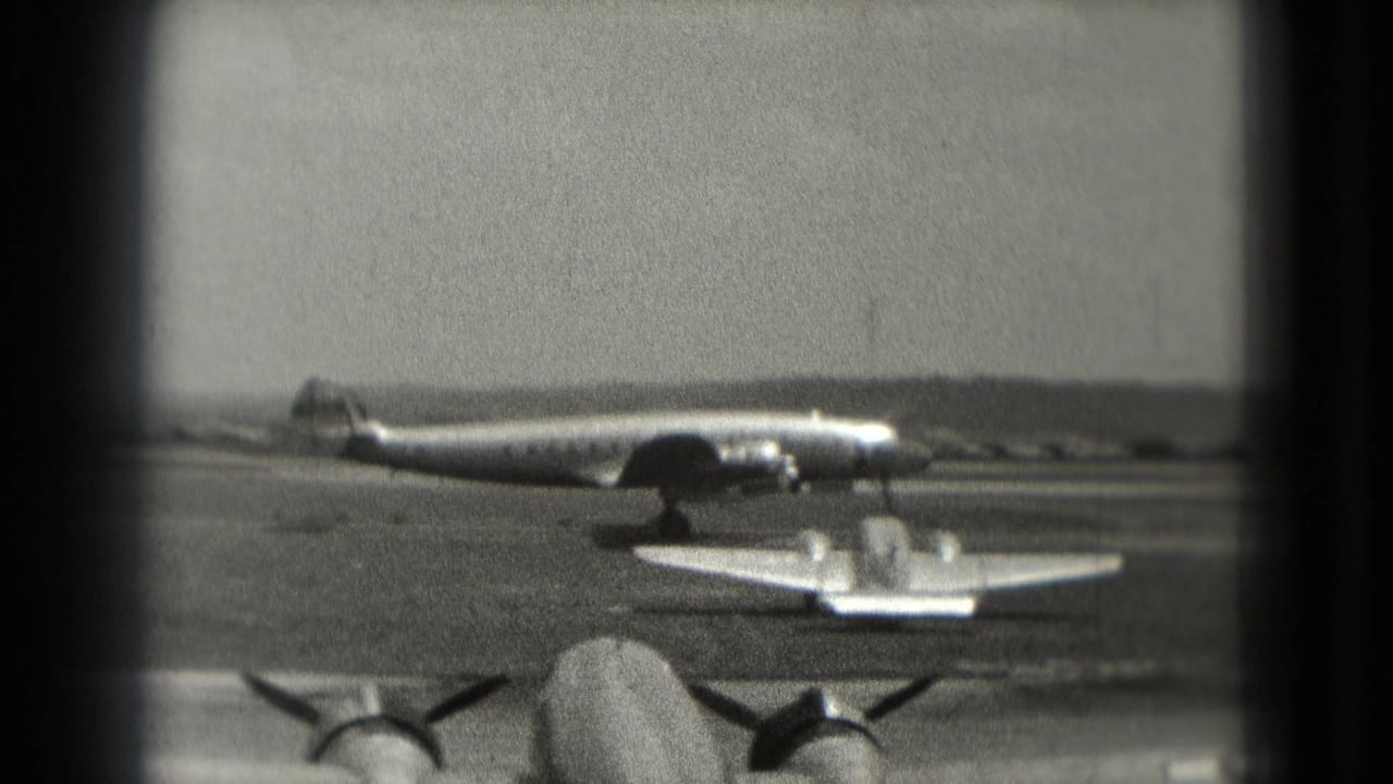 1975 Washington, DC airfield view with a large propeller aircraft, a smaller plane, and foreground aircraft engines in soft 8mm focus.