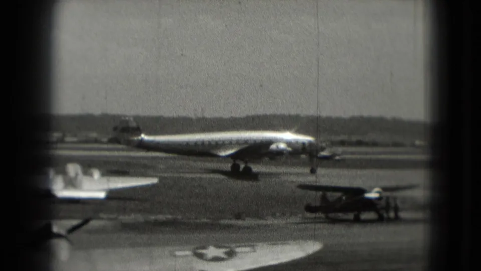 1975 Washington, DC airport view with a propeller aircraft on the runway, a small aircraft at right, and marked aircraft parts in the foreground.