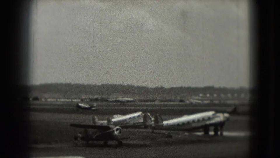 1975 Washington-area airport view with a propeller aircraft, service stairs, distant planes, and dark window-like borders.