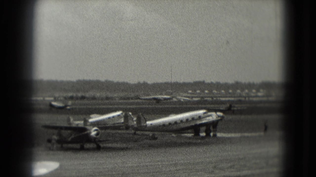 Vintage propeller aircraft appears parked on a Washington, DC area airfield ramp in grainy 1975 8mm footage, with distant ground activity.