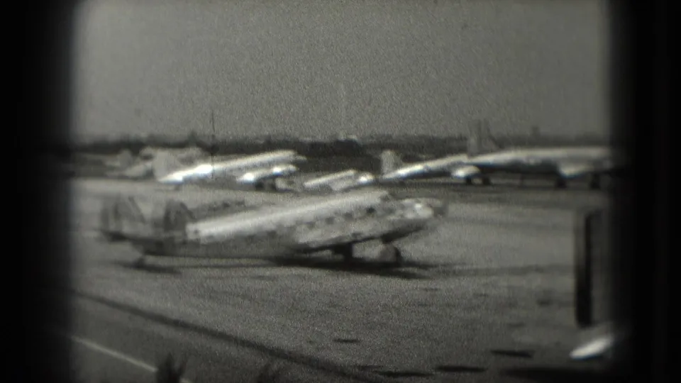 A twin-tail propeller aircraft is parked among other vintage planes on a Washington, DC area airfield in grainy 1975 8mm footage.