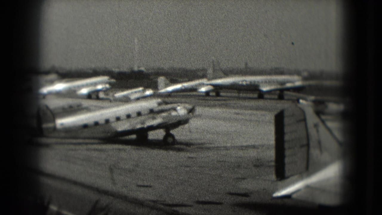 Parked small passenger planes seen across an airport tarmac through a dark frame.