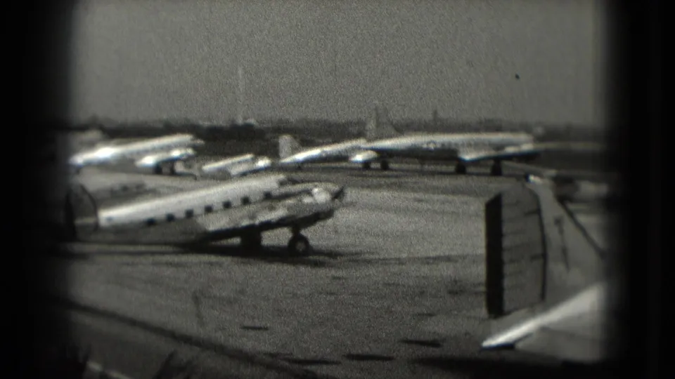 Black-and-white 8mm view of small passenger aircraft parked on a Washington, DC airport tarmac in 1975, seen through a dark window-like frame.