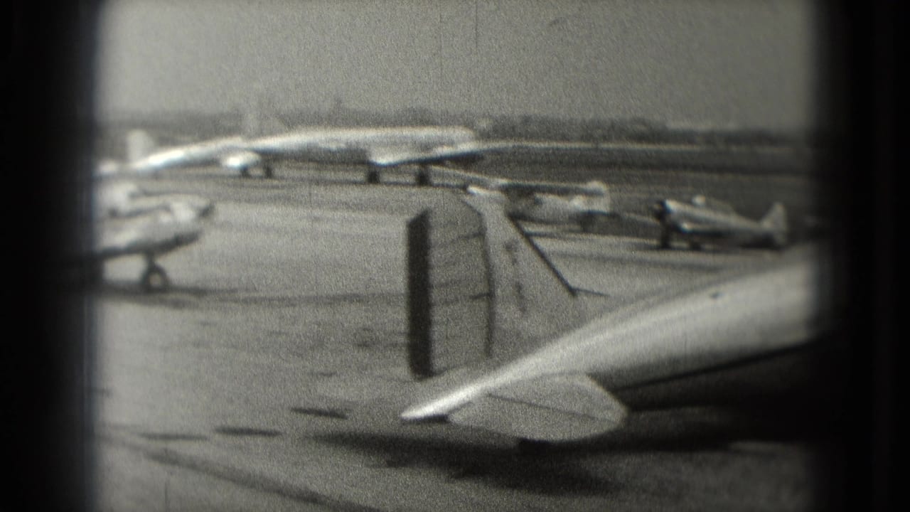 1975 black-and-white home-movie frame showing several small planes parked on a Washington, DC airport ramp, partly obscured by a vertical divider.