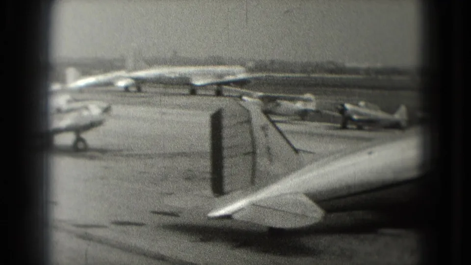 1975 black-and-white home-movie frame showing several small planes parked on a Washington, DC airport ramp, partly obscured by a vertical divider.