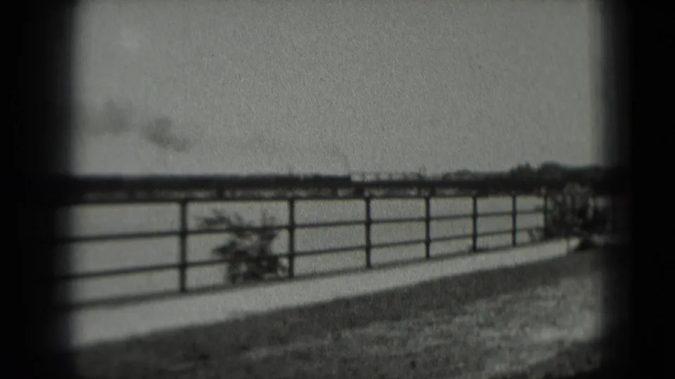 Black-and-white 1975 8mm frame from a Washington, DC-labeled reel showing a fence, open landscape, and distant smoke near a rail line.