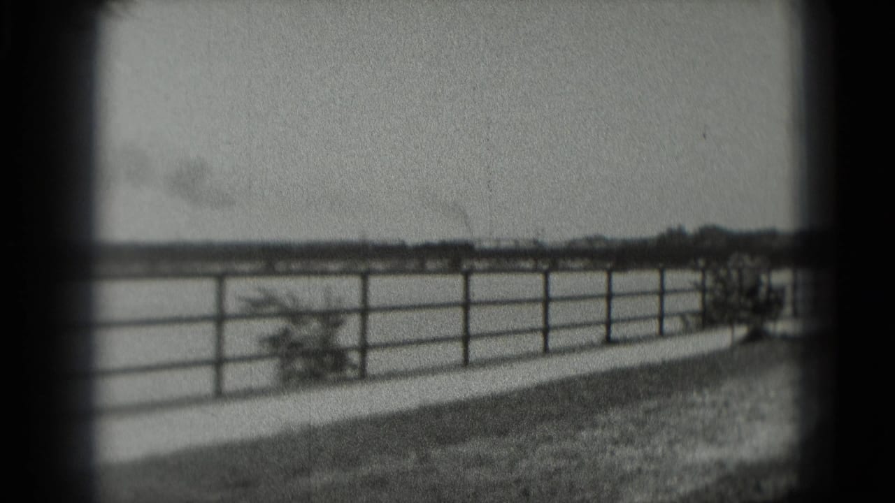 Fence and open landscape with a faint smoky train or rail line in the distance.