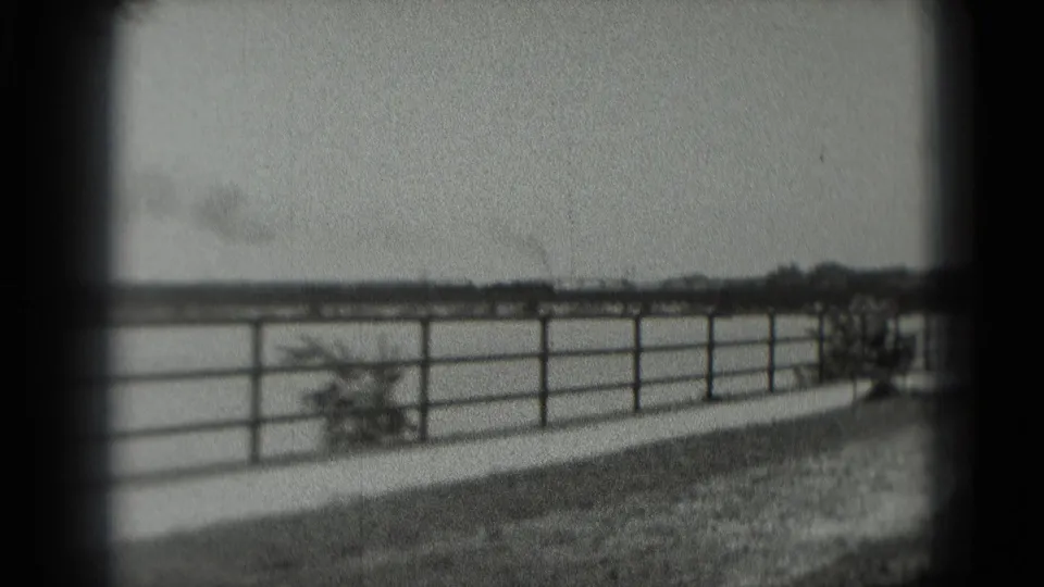 Black-and-white 8mm view of a fenced open area with a low horizon and distant smoke, from metadata-labeled Washington, DC footage.