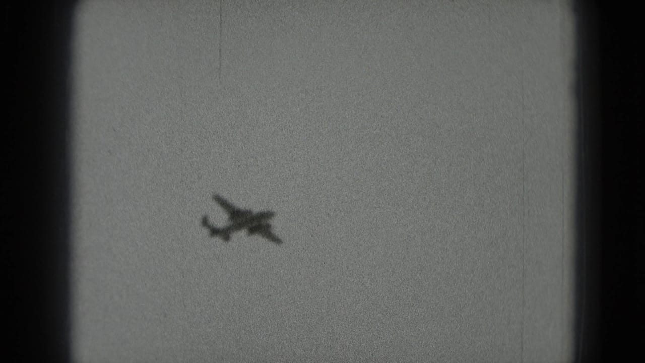 A distant small propeller plane appears against a pale sky in 1975 black-and-white 8mm footage from Washington, DC metadata.