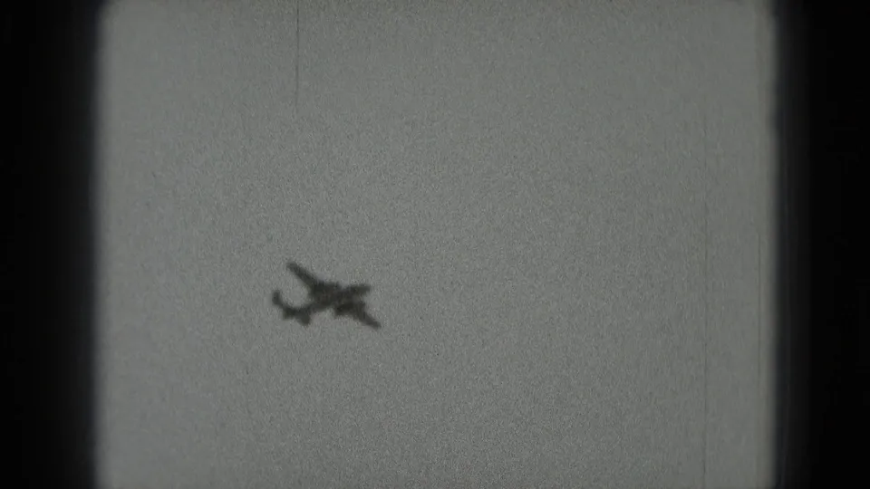 A distant small propeller plane appears against a pale sky in 1975 black-and-white 8mm footage from Washington, DC metadata.