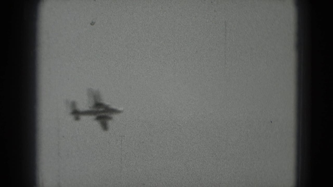The aircraft silhouette is slightly larger and soft against the sky, with visible 8mm grain and dark frame borders.