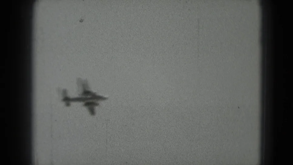The aircraft silhouette is slightly larger and soft against the sky, with visible 8mm grain and dark frame borders.
