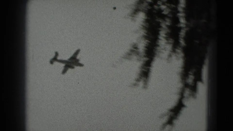 A small propeller plane passes near soft tree silhouettes, adding ground-level context to the black-and-white 8mm view.