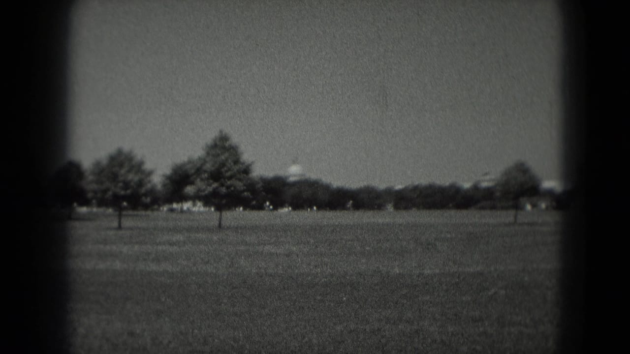 1975 Washington DC home-movie frame looking across a broad lawn toward trees and a distant white domed civic building.