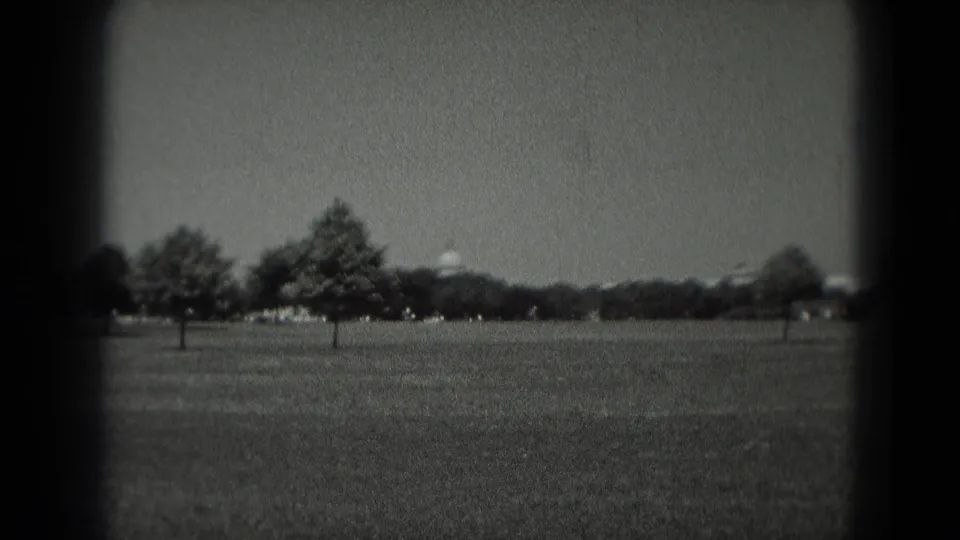 1975 Washington DC home-movie frame looking across a broad lawn toward trees and a distant white domed civic building.