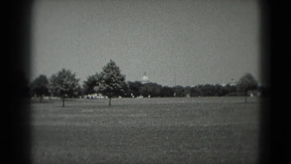 1975 Washington DC frame with a broad grassy foreground, several trees, and a distant white domed building under a bright sky.