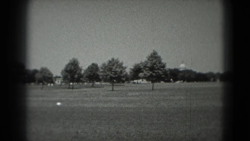 1975 Washington DC 8mm frame showing a tree-lined open lawn with a distant white domed building near the horizon.