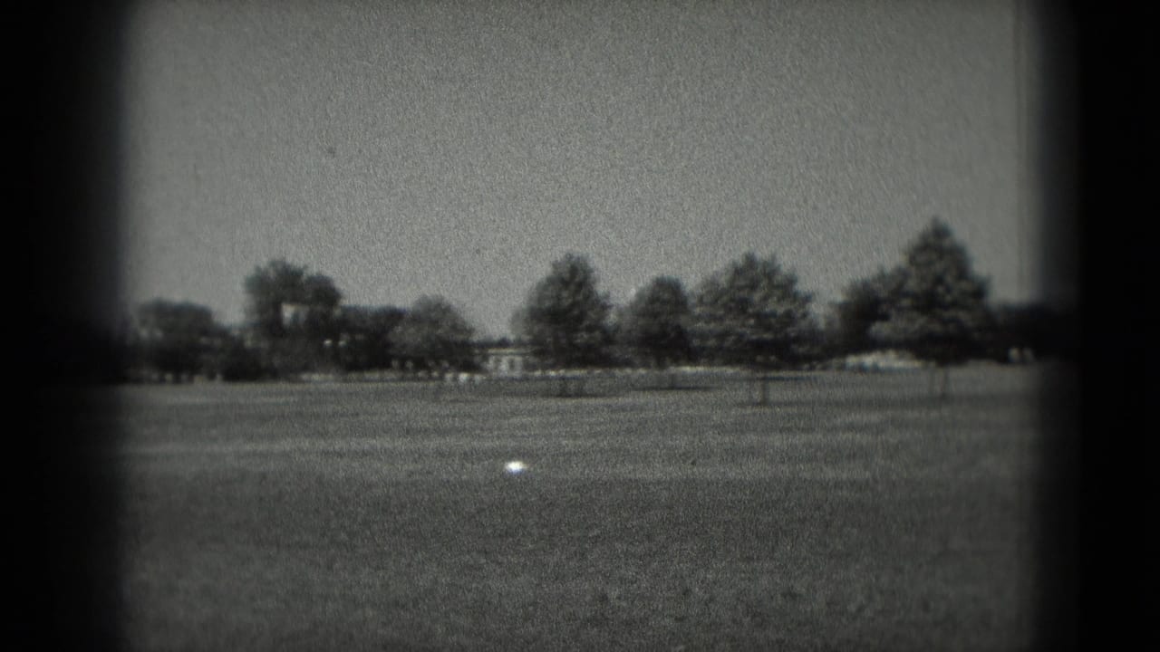 1975 Washington, DC 8mm frame showing an open grassy field, distant tree line and a small pale object in the foreground.