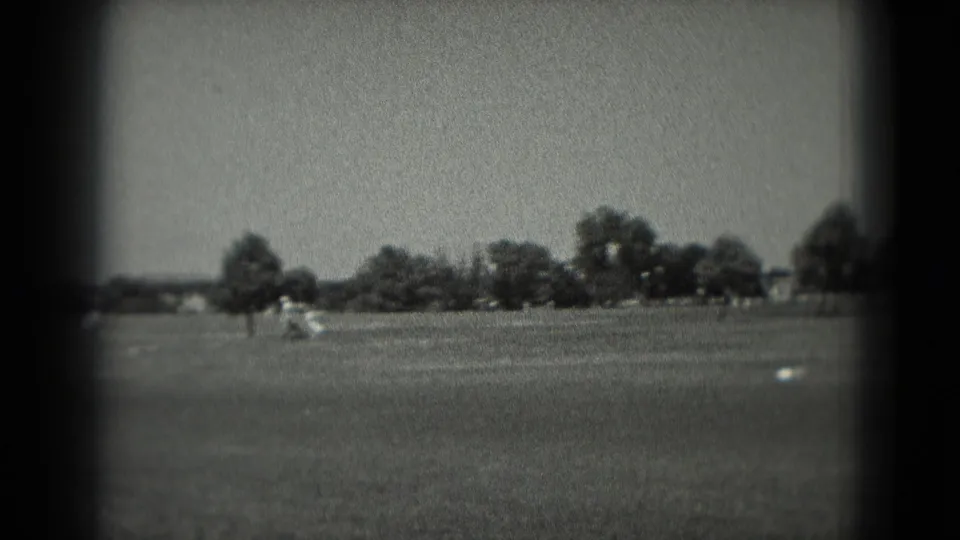 1975 Washington, DC home-movie frame with a grassy park-like field, distant visitors and trees across the horizon.