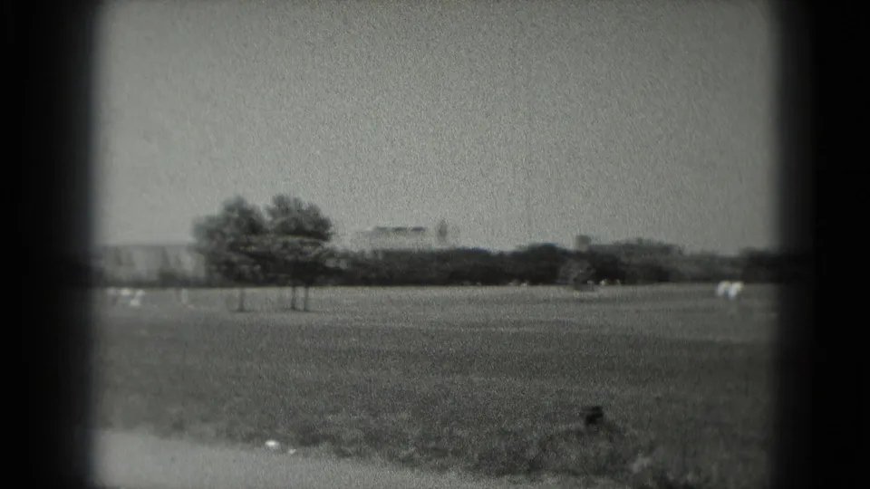 1975 Washington, DC 8mm frame showing a park-like field, trees, faint distant buildings and small pale objects on the grass.