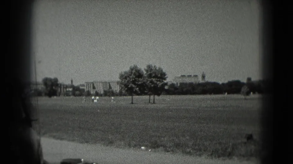 1975 Washington, DC home-movie frame showing an open grassy area, trees, distant buildings, and soft film edges.