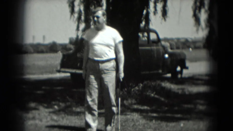 1975 Washington, DC home-movie frame of a man with a golf club beside a tree and parked pickup truck.