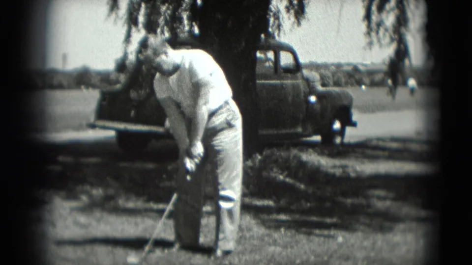The golfer continues setting up his shot in a shaded outdoor Washington, DC scene with a vintage-looking car nearby.
