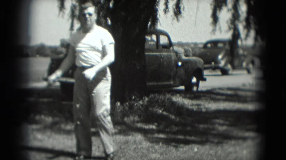 After the swing, the man stands in a sunny Washington, DC roadside scene with a parked older car and another vehicle passing behind.