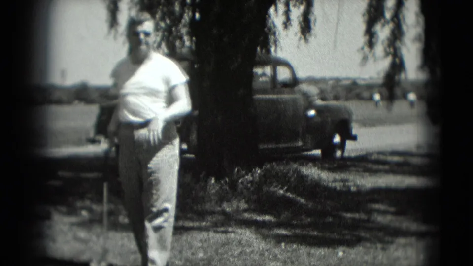 In Washington, DC 1975 home-movie footage, a man stands on a grassy recreation area with a golf club and older cars in the background.