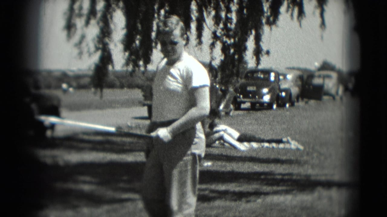 The man holds a golf club in a 1975 Washington, DC recreation scene, with a sunbather on a blanket and parked older cars behind him.