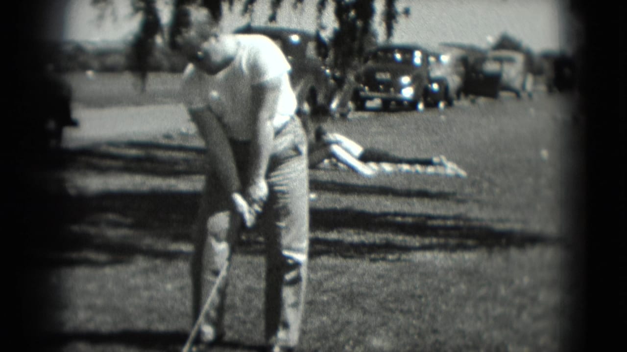 The golfer prepares his swing in a Washington, DC outdoor scene, with mid-1970s cars and a person lying on a blanket behind him.