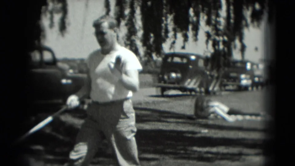 1975 Washington DC 8mm frame showing a man with a golf club on a grassy course, with parked cars and drooping tree branches in the background.