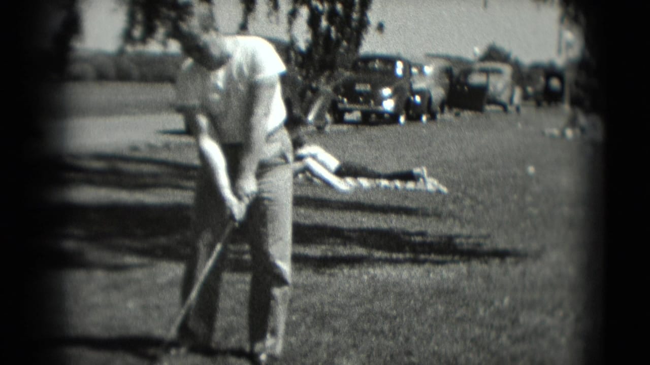 In 1975 Washington, DC home-movie footage, a man stands with a golf club on grass as parked automobiles and a reclining person appear behind him.